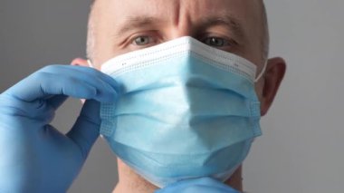 Yüzüne maske takan lateks koruyucu eldivenli kendine güvenen genç bir cerrah. Tıbbi eldivenli profesyonel doktor koruyucu yüz maskesi taktı. Coronavirus COVID-19 video