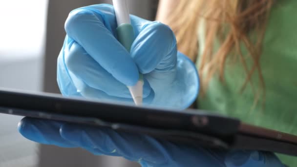 Доктор в перчатках держит планшет и пишет белой ручкой — стоковое видео
