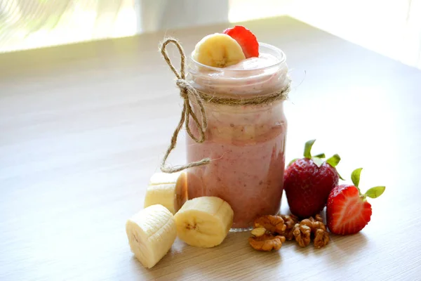Smoothies with bananas, strawberries and nuts on the light background
