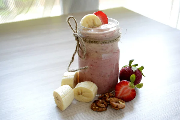 Smoothies with bananas, strawberries and nuts on the light background