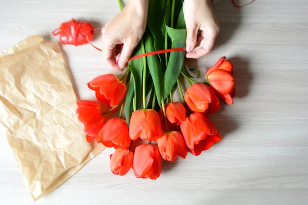 Female hands make a bouquet of red tulips on a wooden background. Spring flowers. Mother\'s day, Valentine\'s day, international women\'s day, March 8