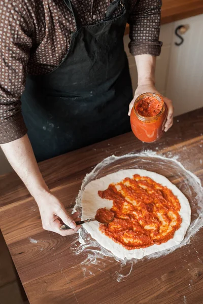 Man Ett Förkläde Matlagning Pizza Vapen Sätter Tomatpuré Degen Vertikal — Stockfoto