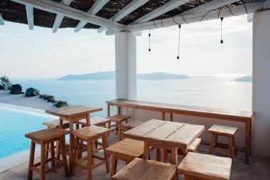 Ahşap masa ve sandalyeler Santorini Adası yüzme havuzunda yanında deniz manzaralı çatı altında Teras