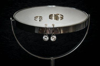 Küpelerin ve alyansların siyah arka planda olduğu ayna..