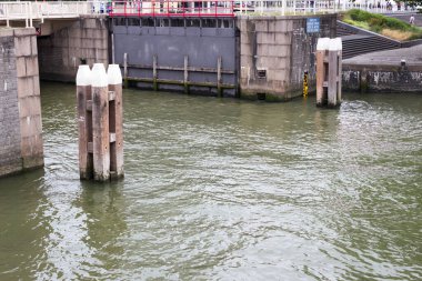 Amsterdam Ren Kanalı 'nın su trafiğini yönetmek için kullanılan altyapıyı vurgulayan, ahşap sütunlar ve sakin suların yer aldığı bir nehir kilidi manzarası