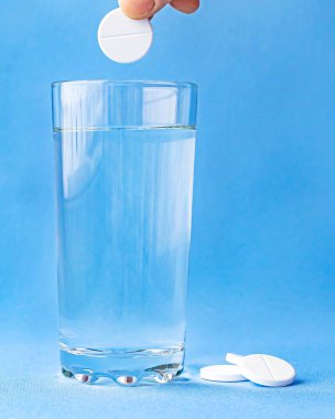 Mavi arka planda bir bardak suda köpüklü aspirin. Dikey biçim ve yumuşak odak.