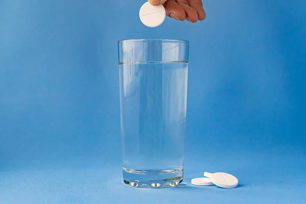 Mavi arka planda bir bardak suda köpüklü aspirin. Dikey biçim ve yumuşak odak.