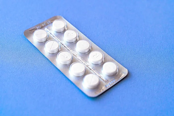 Üstü su toplamış bir aspirin. Çantada C vitamini hapları. Mavi arka planda, yumuşak odaklı beyaz tabletler.. 