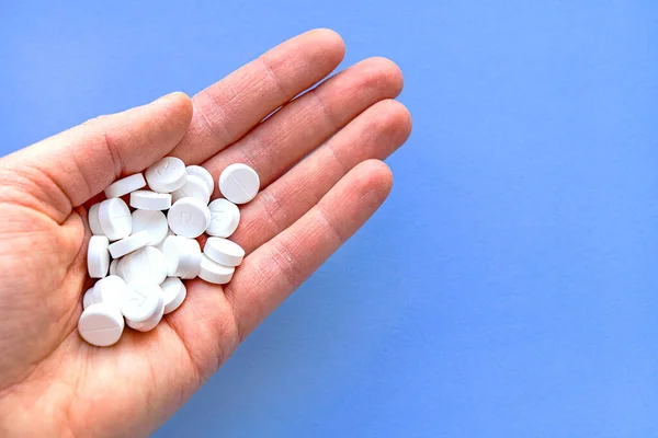 Un puñado de pastillas blancas en la mano sobre un fondo azul . — Foto de Stock