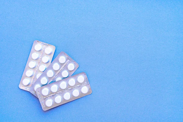 Üstü su toplamış bir aspirin. Çantada C vitamini hapları. Mavi arka planda, yumuşak odaklı beyaz tabletler.. 