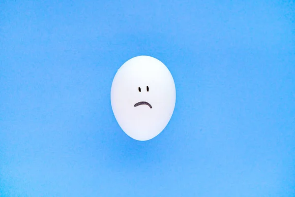 Smutný smajlík na osamělém vejci na modrém pozadí. Zavřít. — Stock fotografie