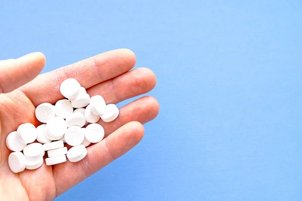 Un puñado de pastillas blancas en la mano sobre un fondo azul . — Foto de Stock