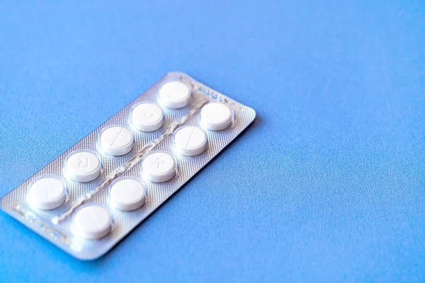 Üstü su toplamış bir aspirin. Çantada C vitamini hapları. Mavi arka planda, yumuşak odaklı beyaz tabletler.. 