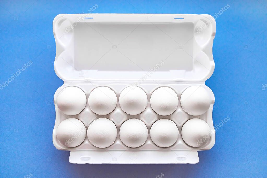 White eggs in a package on a blue background close-up view from above. 