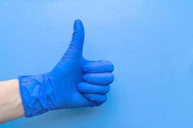 Mavi eldivenli bir el, mavi arka planda harika bir işaret gösteriyor. Metin için boşluk.