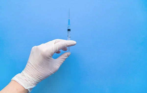 코로나 바이러스 백신을 포함하는 주사기는 흰색 장갑을 낀 손에 의해 파란색 배경에 가까이 붙어 있다. 원문을 위한 공간. — 스톡 사진