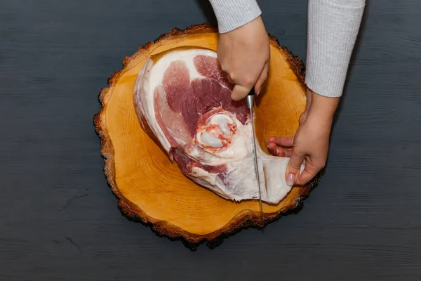 Butchering pig meat, female hands. Raw pork leg on wooden cutting board ready for cooking.