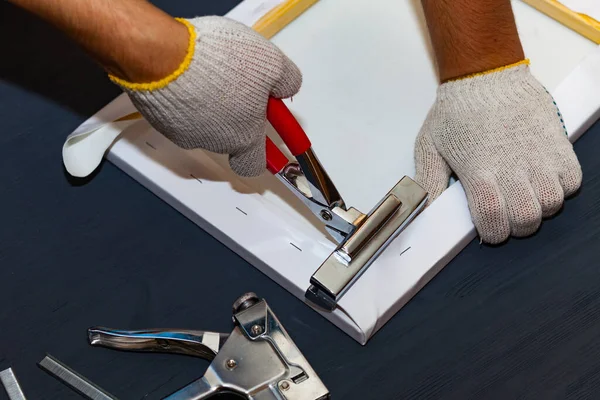 Canvas stretching. Wooden stretcher bar, staple gun, canvas pliers, male hand in white protect glove