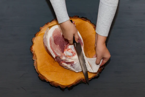 Butchering pig meat, female hands. Raw pork leg on wooden cutting board ready for cooking.