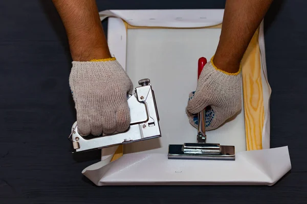 Canvas stretching. Wooden stretcher bar, staple gun, canvas pliers, male hand in white protect glove