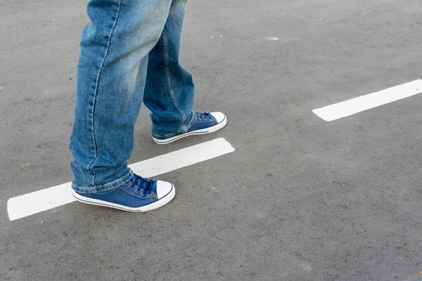 Men\'s feet on the asphalt. A man walks along the road markings