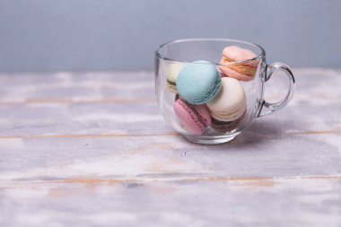 Çok renkli macaroons gri-mavi arka plan üzerinde bir cam fincan. Kopya spase.