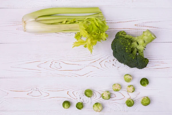 Vista superior de brócolis frescos, couves de Bruxelas e aipo em uma mesa de madeira branca. Conceito vegetariano. Lugar para texto . — Fotografia de Stock