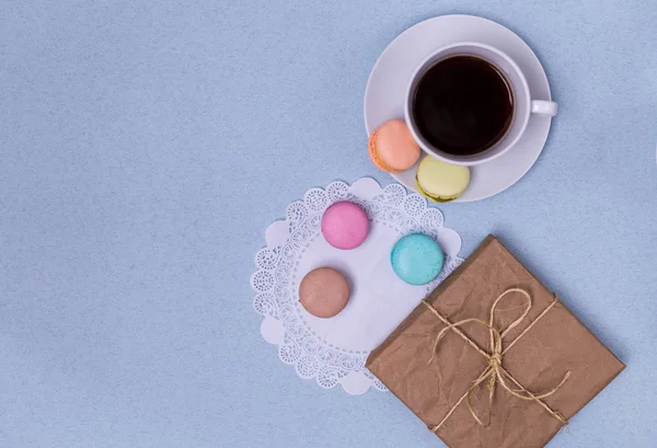 सुबह कॉफी का कप, केक मैकरॉन, उपहार या ऊपर से नीली मेज पर वर्तमान बॉक्स। सुंदर नाश्ता। फ्लैट ले शैली — स्टॉक फ़ोटो, इमेज