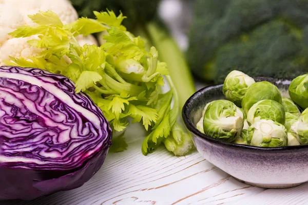 Närbild av blandade färska grönsaker på en vit träbord: kål, broccoli, blomkål och brysselkål och röd kål-ekologiska produkter — Stockfoto