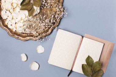 Eski bir tepside beyaz gül yaprakları ve mavi bir masada boş bir günlük. Düz konum, metin için boşluk.