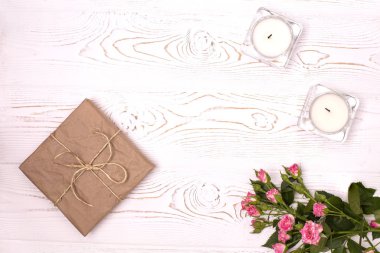 Kraft kağıdına sarılı bir hediye kutusu ve bir çiçek yukarıdan beyaz ahşap bir arka planda mumlar. Düz yatıyordu.