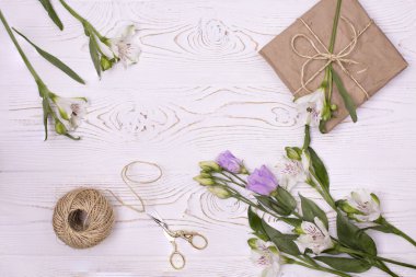 Kraft kağıdı ve çiçeğe sarılı hediye kutusu yukarıdan beyaz ahşap bir arka planda sicim ve makas. Düz yatıyordu