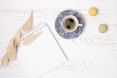 Yaylı boş bir günlükten kompozisyon, bir fincan kahve, badem kurabiyesi ve bej yapraklar beyaz eski püskü ahşap bir masada. Moda düzlüğü