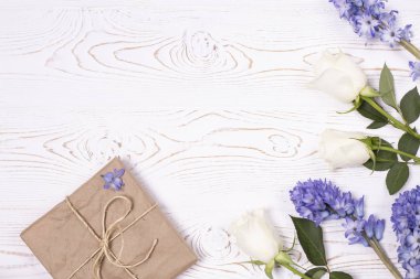 El işi kağıdına sarılı bir hediye kutusu ve mavi sümbül çiçekleri, beyaz bir masanın üstünde beyaz güller. Düz yatıyordu. Metin için alanı kopyala.