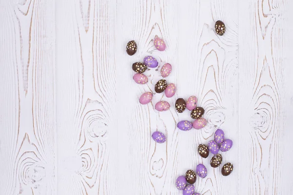 Vista superior de ovos de chocolate de Páscoa coloridos em papel alumínio rosa, marrom e roxo em uma mesa de madeira rasgada branca . — Fotografia de Stock