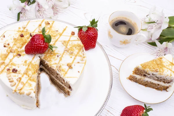 白盘上有奶油和坚果，草莓多汁，桌上有咖啡和鲜花的蛋糕. — 图库照片