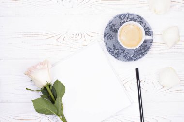 Kahve fincanının üst görüntüsü, boş not defteri, kalem, beyaz masadaki çiçekler. Düz yatıyordu.