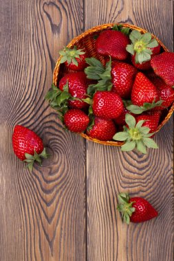Kahverengi, köhne, ahşap bir masada hasır bir kasede sulu çileklerin üst görüntüsü.