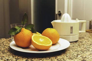 Meyve sıkacağı taze sıkılmış portakal suyu ve bütün ve dilimlenmiş portakallar mutfaktaki taş bir masada..