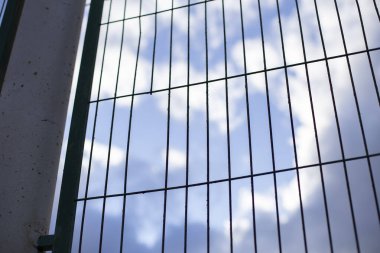 Parmaklıklı çit. Çitin arkasında bulutlu mavi gökyüzü. Sonuç konsepti, göç. Boşluğu kopyala.