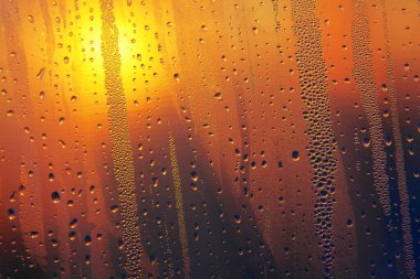 Arka planda günbatımı olan bardağa damlalar