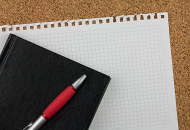 Boş kare beyaz kağıt sayfası metni Not Defteri'nden wrested. Siyah defter, kırmızı kalem ve mantar pano arka plan vardır.