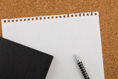 Boş kare beyaz kağıt sayfası metni Not Defteri'nden wrested. Siyah defter, siyah kalem ve mantar pano arka plan vardır.