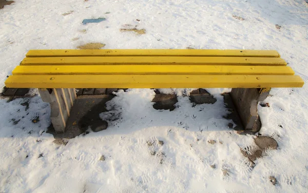 Ξύλινο κίτρινο πάγκο στο πάρκο που περιβάλλεται από χιόνι — Φωτογραφία Αρχείου