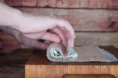 Maki sushi yapma işlemi. Peynir, salatalık ve susam rulo romaji maki sudare ile ahşap tahta üzerinde hazırlanıyor Şef eller yemek