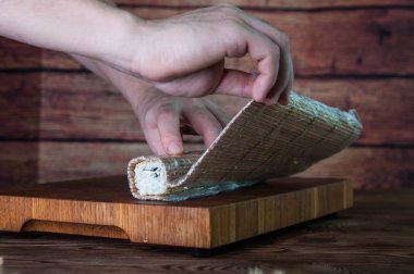 Maki sushi yapma işlemi. Peynir, salatalık ve susam rulo romaji maki sudare ile ahşap tahta üzerinde hazırlanıyor Şef eller yemek