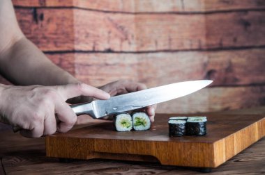 Maki sushi yapma işlemi. Peynir, salatalık ve susam rulo romaji maki sudare ile ahşap tahta üzerinde hazırlanıyor Şef eller yemek