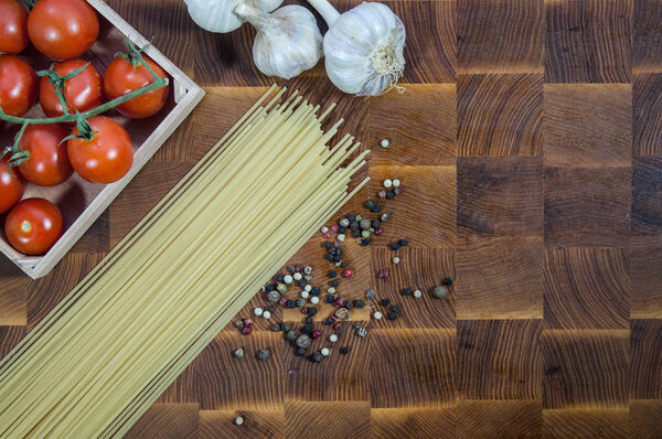 Fresh healthy italian food ingredients - pasta spaghetti, garlic, cherry tomatoes and pepper on wooden cutting board with place for text top view flat lay