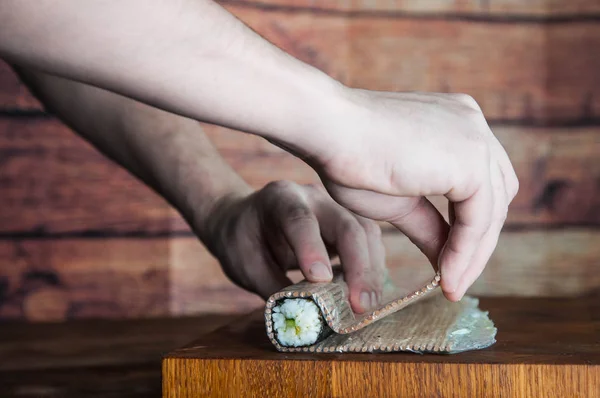 Process of making maki sushi. Cook chef hands preparing rolls with cheese, cucumber and sesame seeds on wooden board with romaji maki sudare