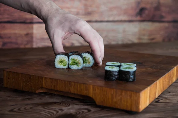 Process of making maki sushi. Cook chef hands preparing rolls with cheese, cucumber and sesame seeds on wooden board with romaji maki sudare